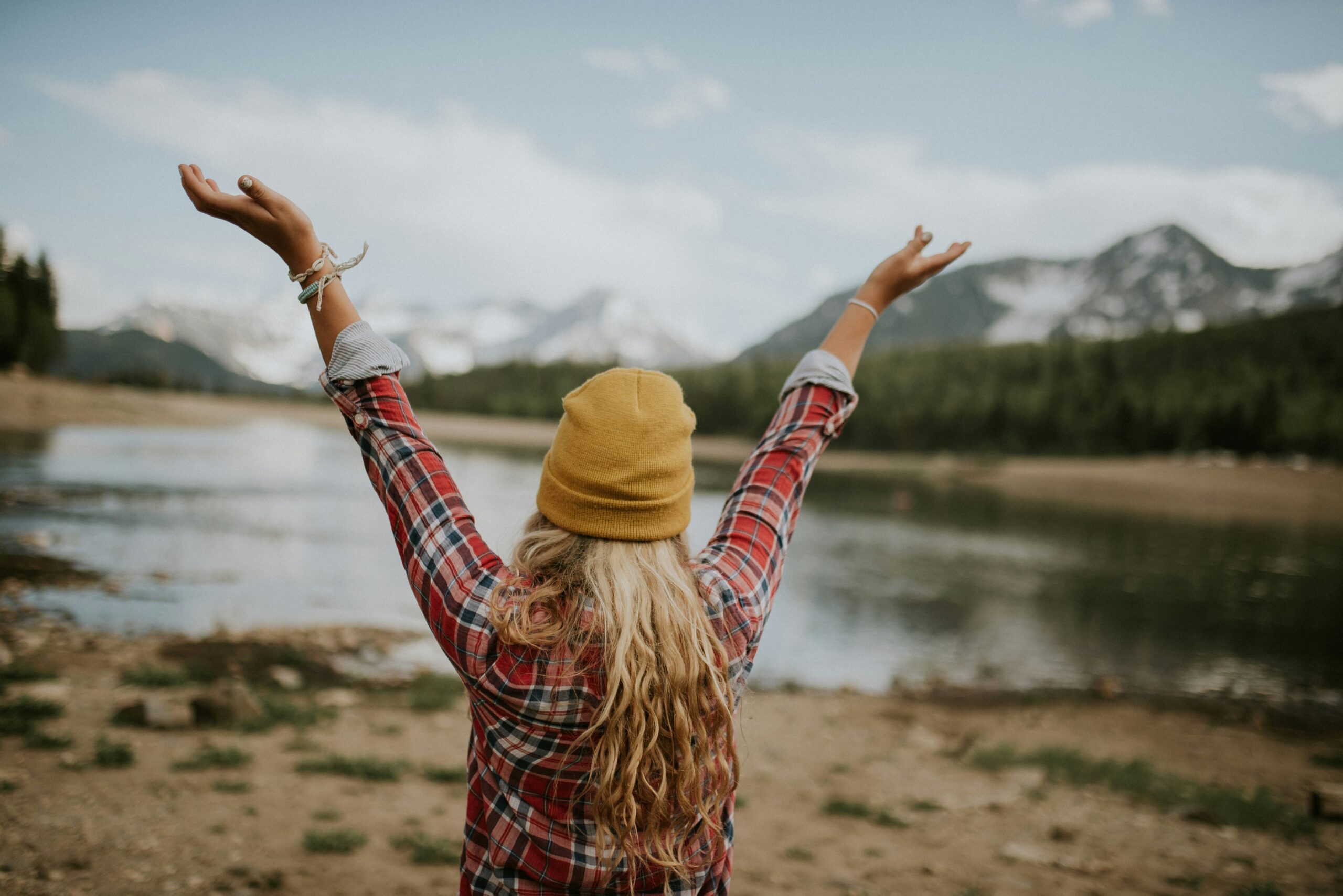 Woman standing with arms raised in a picturesque mountain landscape, symbolizing financial freedom and the joy of overcoming debt.